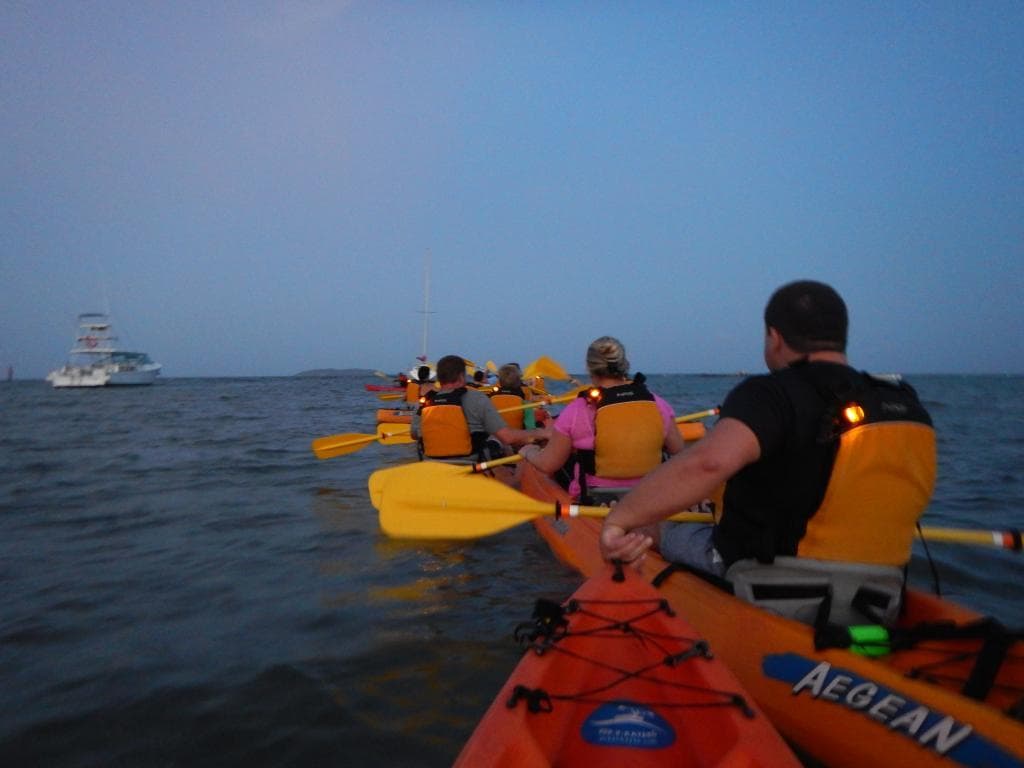 Guided sea kayaking excursion paddling toward open ocean sunset