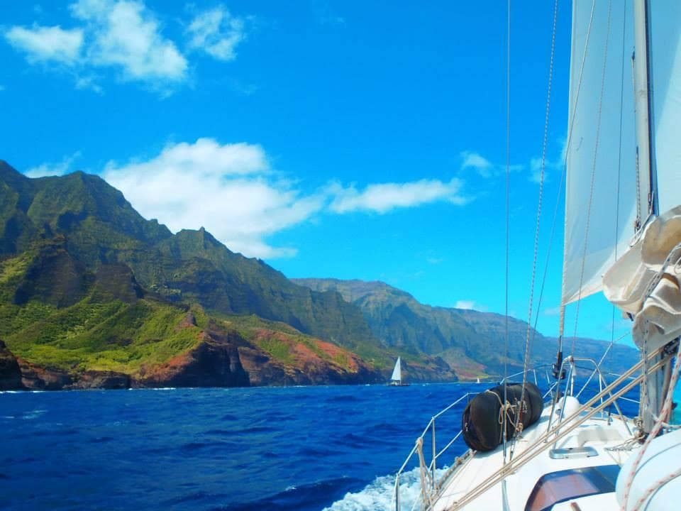 Sailboat cruising along lush coastal cliffs under blue sky
