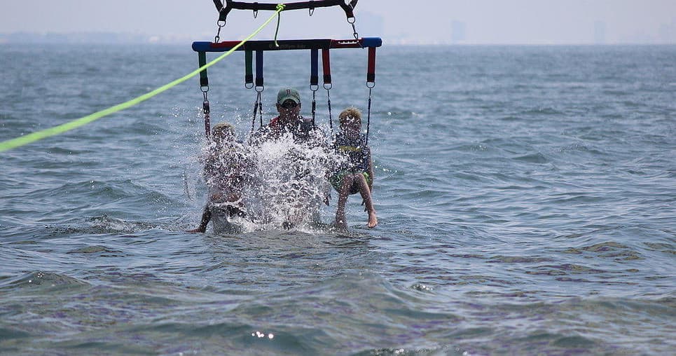 Two people parasailing skimming ocean surface with water splash