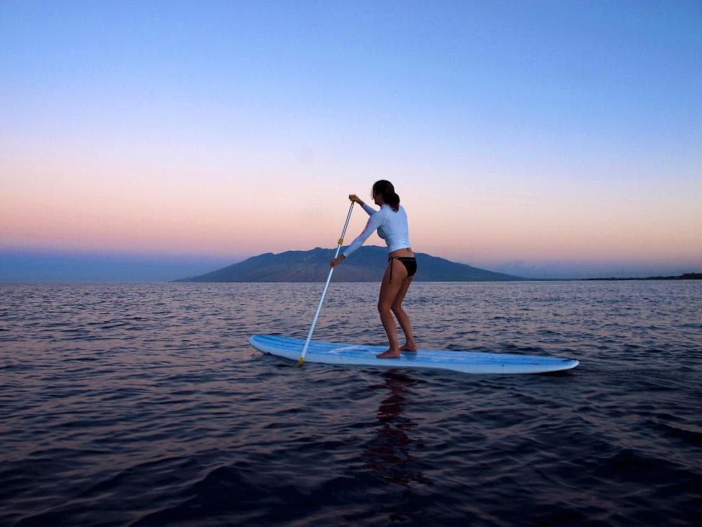 Solo paddleboarder at sunset on calm Maui ocean horizon