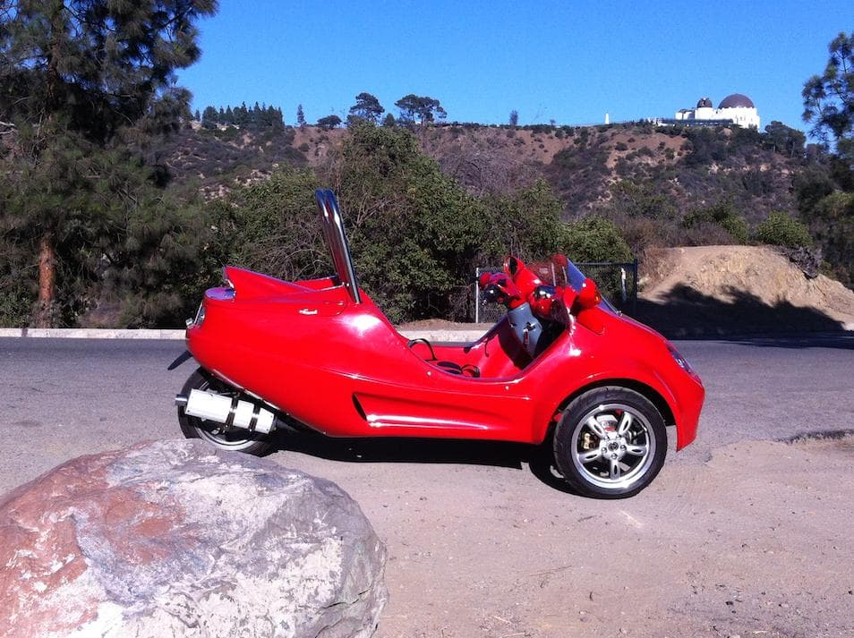 Red three-wheeled scooter parked with observatory hill view