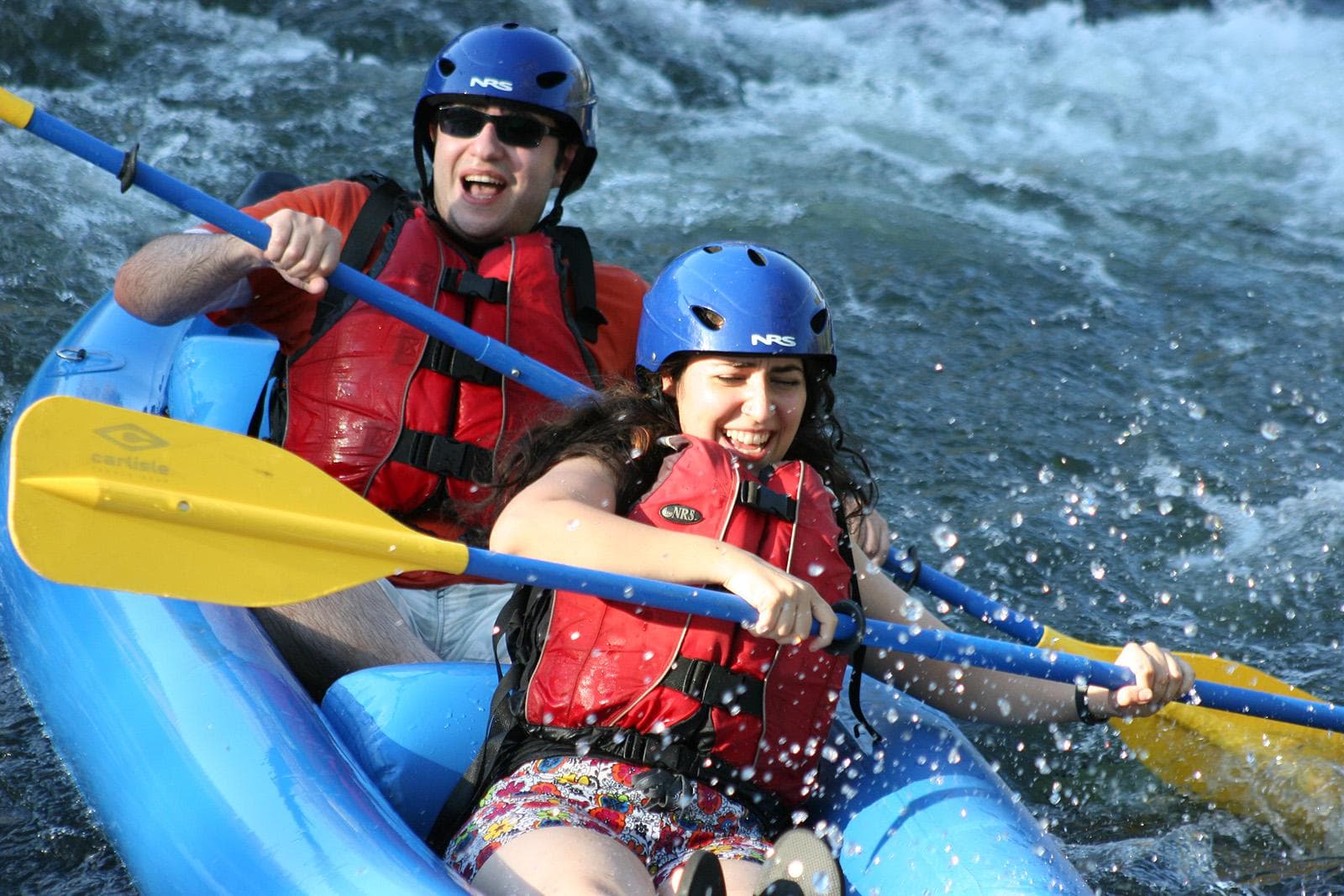 Two paddlers in blue raft navigating fast river rapids with excitement