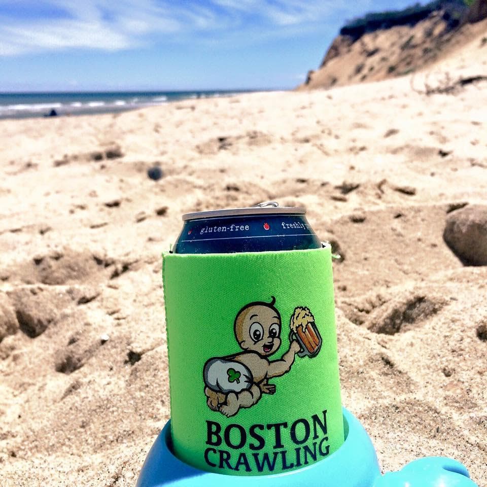 Beach koozie with Boston Crawling logo on sandy coastal beach