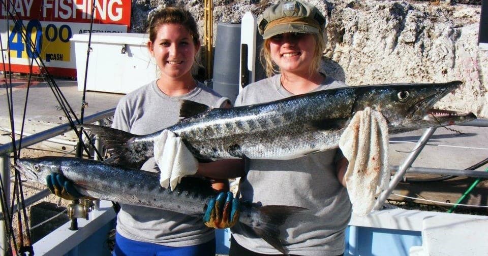 Two anglers holding large barracuda on charter boat dockside