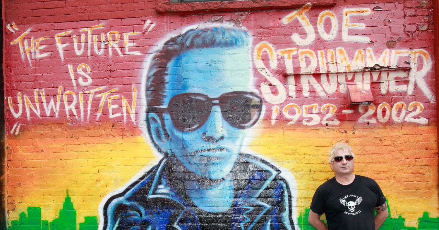 Person standing before Joe Strummer mural on urban brick wall