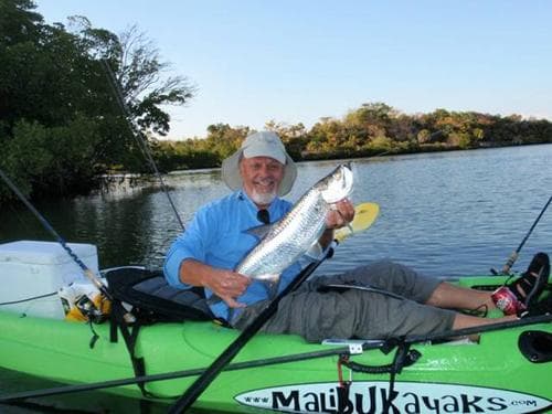 Angler in kayak holding freshly caught fish on calm river
