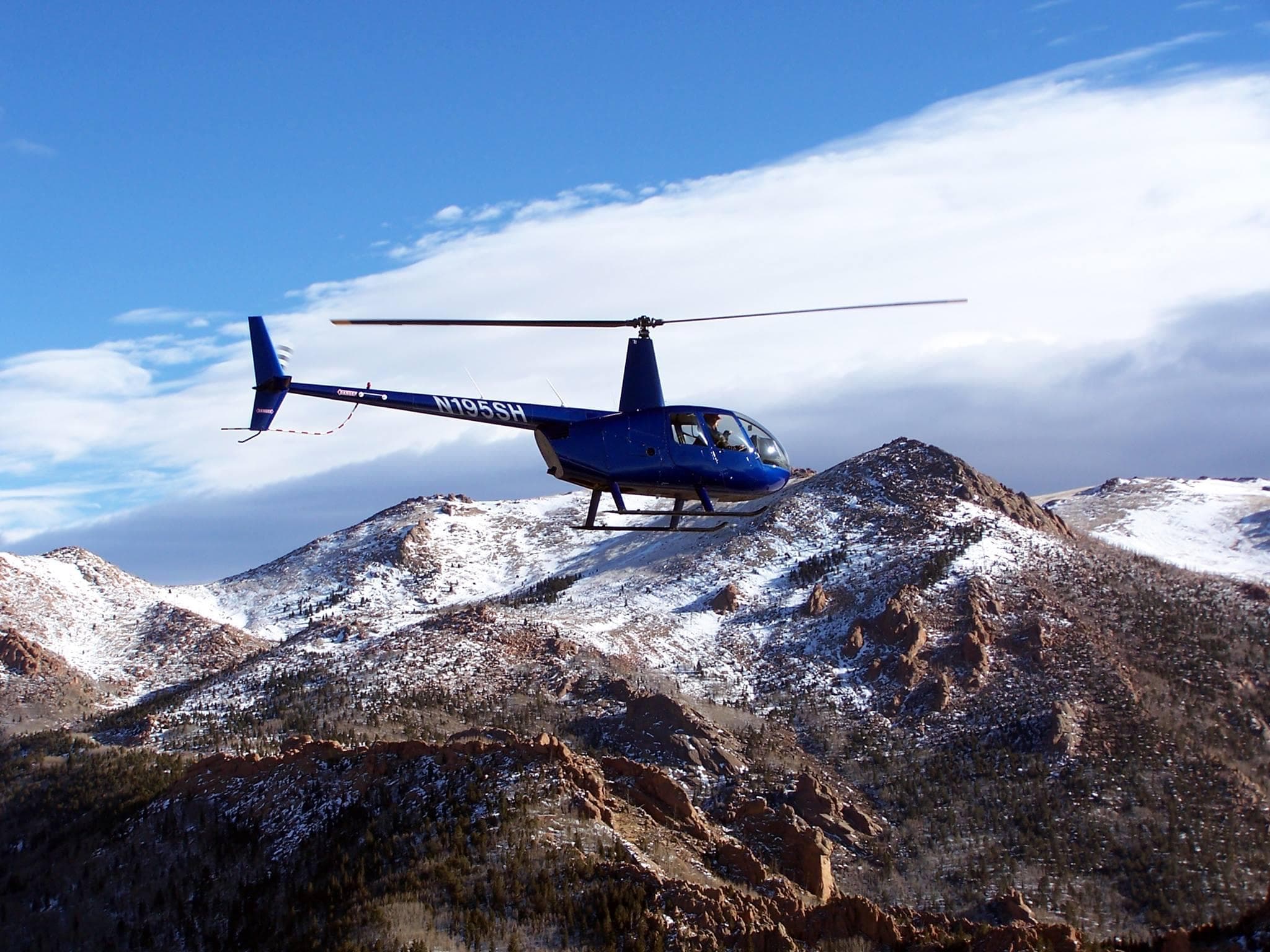 Blue helicopter flying over snowy Colorado mountain ridges