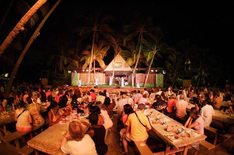 Outdoor beachfront luau audience dining under palm trees at night