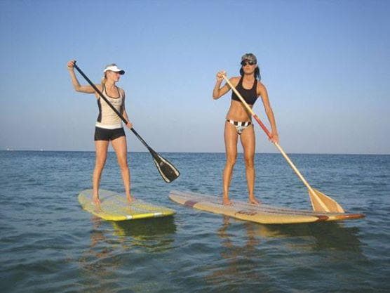 Two women stand-up paddleboarding on calm ocean near horizon