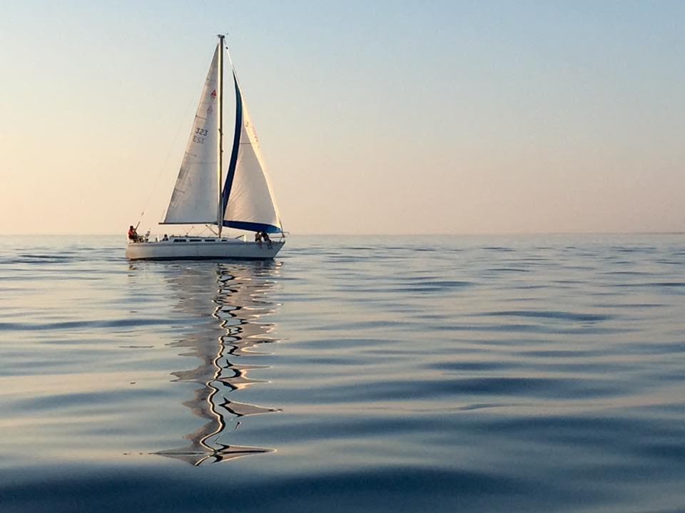 Single sailboat gliding on calm reflective lake at sunrise