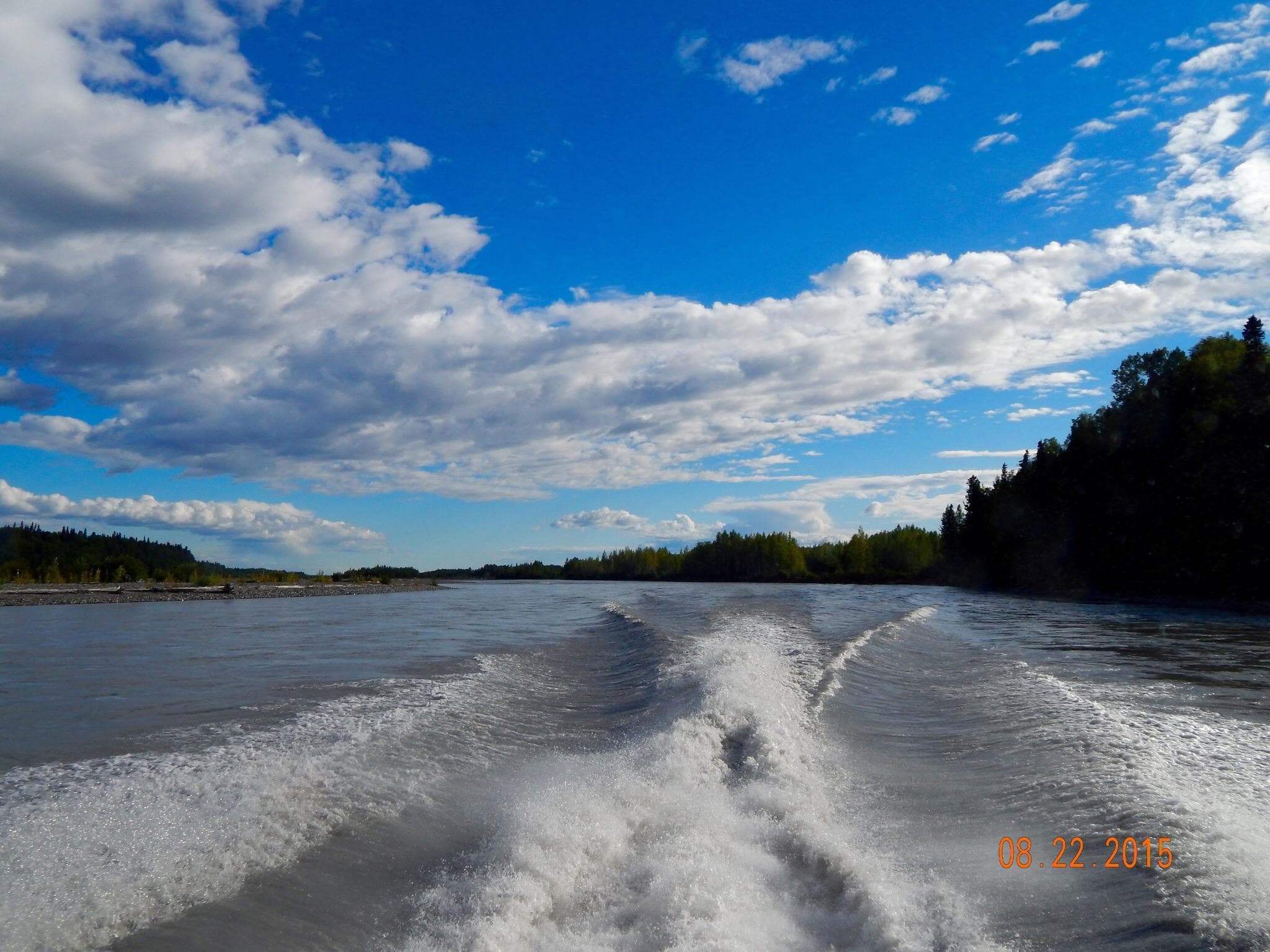 Boat wake trail on river under dramatic blue sky clouds