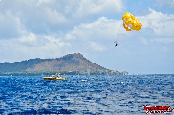 Parasailing over open ocean with coastal mountain backdrop